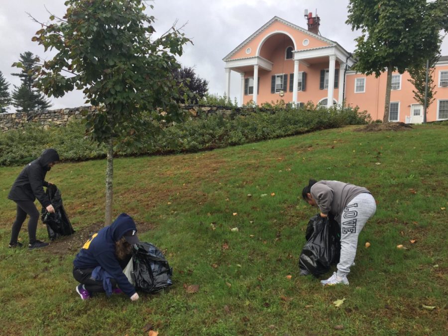 Three students are picking up trash on Choate hill during campus cleanup. 